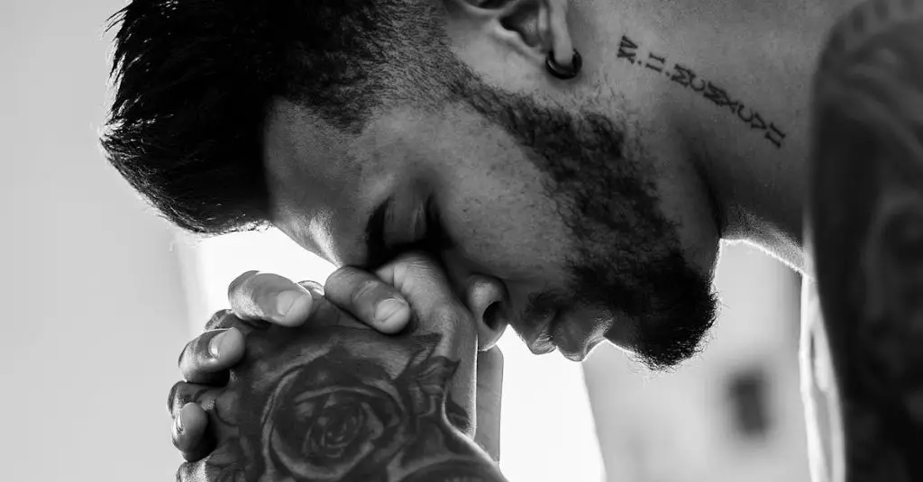 A man in deep thought and prayer, showcasing tattoos and an earring in a powerful black and white image.
